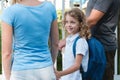 Blonde boy with the blue backpack walks between his parents holding his hands