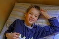 Cute blonde boy in blue pajama smiling, waking up in bed in the morning close-up. Kids bedroom. Relax