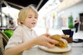 Cute blonde boy eating large bagel with salmon and arugula in outdoor fast food restaurant Royalty Free Stock Photo