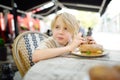 Cute blonde boy eating large bagel with salmon and arugula in outdoor fast food restaurant Royalty Free Stock Photo