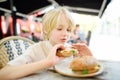 Cute blonde boy eating large bagel with salmon and arugula in outdoor fast food restaurant Royalty Free Stock Photo