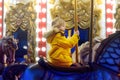 Cute blonde boy enjoying Christmas fair. Little child riding on a vintage carousel merry go round. Outdoors entertainment Royalty Free Stock Photo