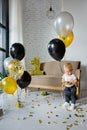 Cute blonde boy on his first birthday at a decorated party in gold, black and silver colors. Playing with balloons Royalty Free Stock Photo