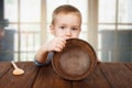 Cute blonde boy shows empty plate, hunger concept