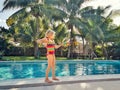 Cute blonde Caucasian young girl standing by swimming pool and playing with water gun. Fun summer outdoor activity for kids. Child Royalty Free Stock Photo