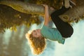 Cute blonde child boy hangs on a tree branch. Summer holidays, little boy climbing a tree. Upside down. Childhood