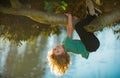 Cute blonde child boy hangs on a tree branch. Summer holidays, little boy climbing a tree. Upside down. Royalty Free Stock Photo