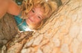 Cute blonde child boy hangs on a tree branch. Summer holidays, little boy climbing a tree.