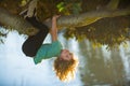 Cute blonde child boy hangs on a tree branch. Summer holidays, little boy climbing a tree. Upside down.