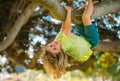 Cute blonde child boy hangs on a tree branch. Summer holidays, little boy climbing a tree. Upside down. Kid boy playing