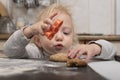 Cute blonde child helps to cook cookies. Little girl makes a gingerbread man from dough