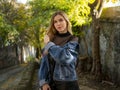 Cute blonde with flowing hair in a denim jacket is standing on the street against a stone staircase in the park Royalty Free Stock Photo