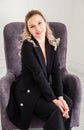 A cute blonde girl in a black suit is sitting in a chair, smiling and looking at the camera Royalty Free Stock Photo