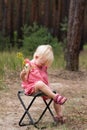 Cute blonde girl sits on picnic chair in the forest. Vertical frame