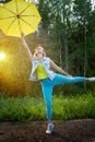 Cute blonde girl with umbrella under rain drops on nature in a sunny summer day. Funny young woman dancing in forest Royalty Free Stock Photo