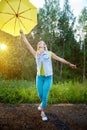 Cute blonde girl with umbrella under rain drops on nature in a sunny summer day. Funny young woman dancing in forest Royalty Free Stock Photo