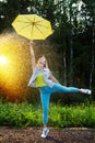 Cute blonde girl with umbrella under rain drops on nature in a sunny summer day. Funny young woman dancing in forest Royalty Free Stock Photo