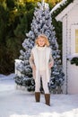 Cute blonde girl under the falling snow near the small house and snow-covered trees. New Year and Christmas time Royalty Free Stock Photo
