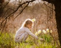 Cute blonde happy little girl with yellow daffodils in the spring country Royalty Free Stock Photo