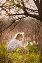 Cute blonde happy little girl with yellow daffodils in the spring country Royalty Free Stock Photo