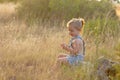 A cute blonde little girl sitting in a meadow at sunset. Royalty Free Stock Photo