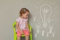 Cute blonde little girl standing on a chair thinking of something. Business ideas and success start small concept Royalty Free Stock Photo