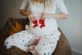 Cute blonde pregnant woman in spotted pyjamas is sitting on the bean bag chair. She is holding small red socks near her belly. Royalty Free Stock Photo