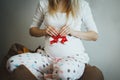 Cute blonde pregnant woman in spotted pyjamas is sitting on the bean bag chair. She is holding small red socks near her belly. Royalty Free Stock Photo