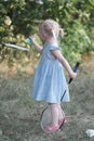 Cute blonde three years old girl with two tails plays badminton. Child in blue dress holds racket and shuttlecock