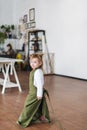 Cute blonde three years old girl in white jacket and green apron is in a creative class.