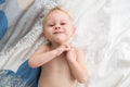 Cute blonde toddler boy lies on bed and smiles.