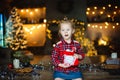 A beautiful little blonde received a sweet Christmas gift and laughs happily sitting on a wooden table in a decorated house Royalty Free Stock Photo