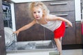 Cute blonde toddler girl helping in the kitchen taking plates out of dish washing machine Royalty Free Stock Photo