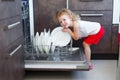 Cute blonde toddler girl helping in the kitchen taking plates out of dish washing machine Royalty Free Stock Photo