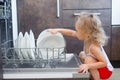 Cute blonde toddler girl helping in the kitchen taking plates out of dish washing machine Royalty Free Stock Photo