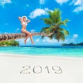 Cute blonde woman at palm tree against tropical ocean beach, season 2019 concept Royalty Free Stock Photo