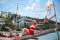 Cute blonde woman in red dress, sunglasses and santa hat sitting on palm tree at exotic tropical beach. Holiday concept Royalty Free Stock Photo