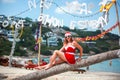 Cute blonde woman in red dress, sunglasses and santa hat sitting on palm tree at exotic tropical beach. Holiday concept Royalty Free Stock Photo