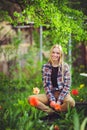 Cute blonde woman sits in a home garden, on a background of lots of green trees and tulips, a beautiful portrait of a rustic style