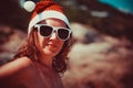 Cute blonde woman in sunglasses and santa hat on at exotic tropical beach in retro colors. Holiday concept for New Years Royalty Free Stock Photo