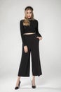 Cute blonde young model posing in chic black blouse and loose pants.