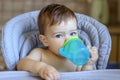 Cute blue-eyed baby boy holding plastic mug in his hands and drinking water itself lookin at camera, Royalty Free Stock Photo