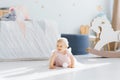 A cute blue eyed blonde one year old baby in a pink dress is holding crawling on all fours in the children`s room on the floor Royalty Free Stock Photo