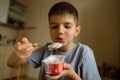 Cute boy with appetite eats yogur with spoon, grimaces. Royalty Free Stock Photo