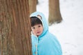 Cute boy in blue cloak playing hide and seek in forest after snow Royalty Free Stock Photo