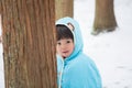 Cute boy in blue cloak playing hide and seek in forest after snow Royalty Free Stock Photo