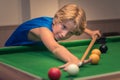 Cute boy in blue t shirt plays billiard or pool in club. Young Kid learns to play snooker. Boy with billiard cue strikes the ball