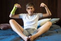 Cute boy with broken hand relaxing and smiling on couch. Close up young handsome Teenage with elbow plaster Royalty Free Stock Photo