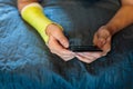 Cute boy with broken hand relaxing and smiling on couch. Close up young handsome Teenage with elbow plaster playing smartphone Royalty Free Stock Photo
