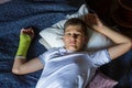 Cute boy with broken hand relaxing and smiling on couch. Close up young handsome Teenage with yellow plaster Royalty Free Stock Photo